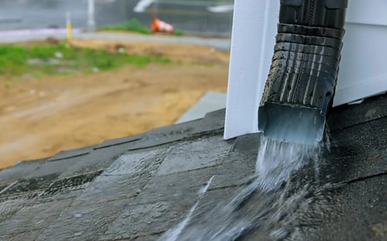 Rainwater discharging from a downspout beside a home foundation during heavy rainfall
