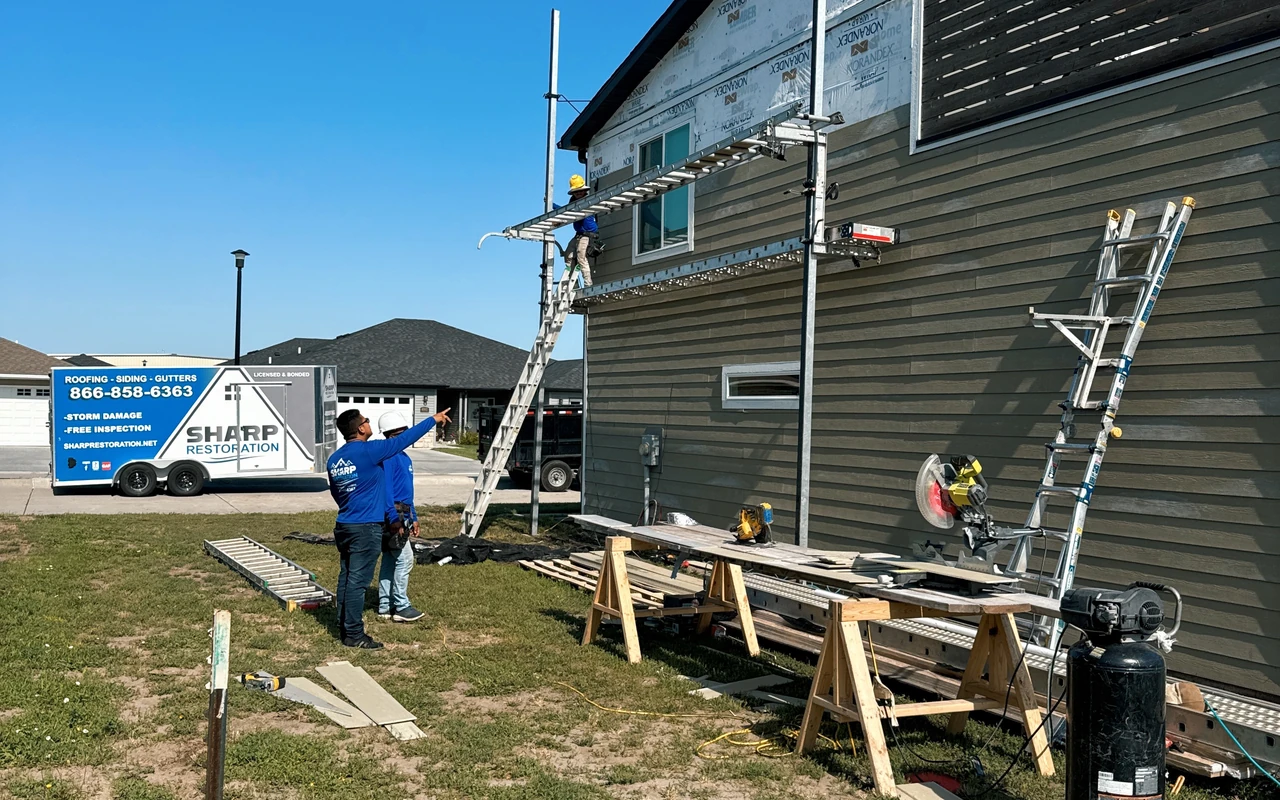 Sharp Restoration crew installing new horizontal siding on a home with ladders and branded trailer on site