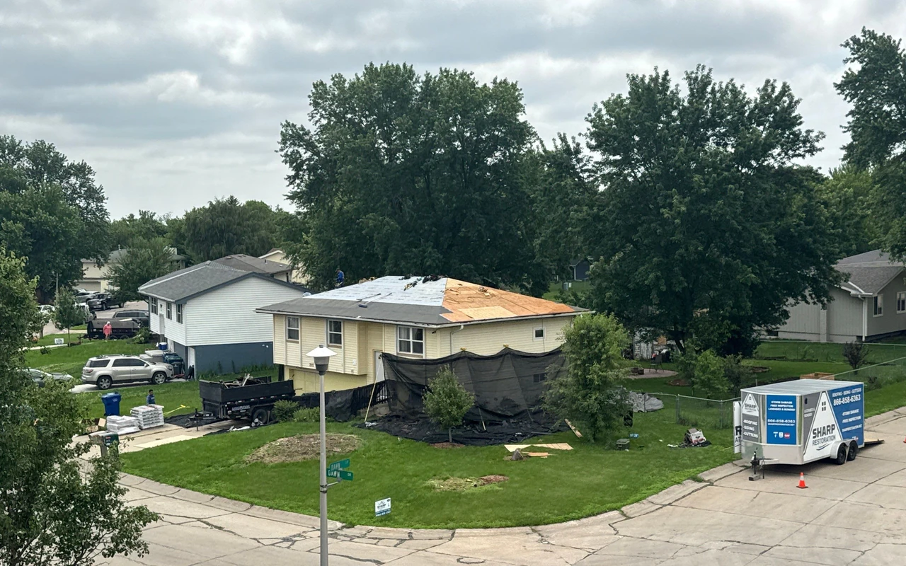 Home with storm-damaged roof under restoration, protective tarps and Sharp Restoration trailer on site